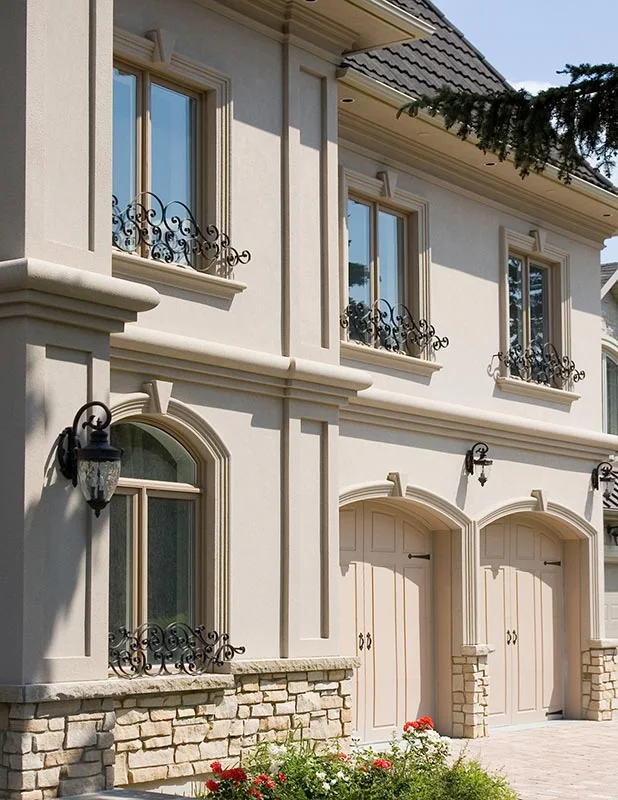 Encadrements de fenêtres et moulures décoratives sur une façade pâle à deux étages.