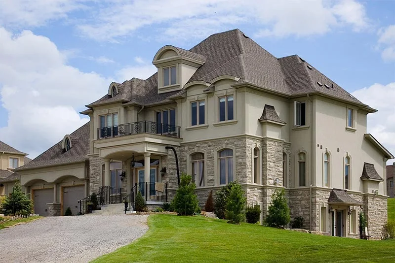 Grande maison avec moulures extérieures pâles et pierre autour des fenêtres inférieures.