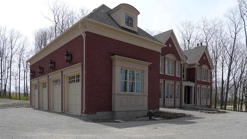 Maison en brique rouge avec coins pâles et moulures autour des portes de garage.